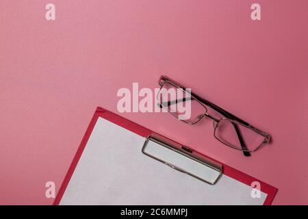 glasses and paper in folder laying isolated on pink background Stock Photo