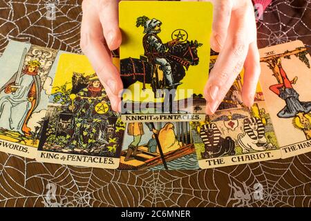 Tarot cards from the 1910 Rider-Waite design. Tarot reading with Knight and Pentacles card held up. Spider web background. Stock Photo