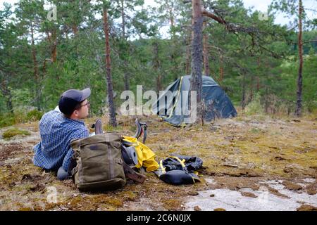 Man relaxing after outdoor activity near tent smiling enjoying nature. Stock Photo