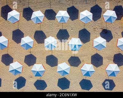 Pattern of white umbrellas on the sand. Sunny beach and long morning shadows from umbrellas. Stock Photo