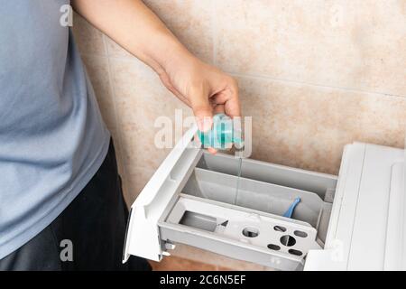 Person pouring concentrated compact laundry liquid detergent into washing machine to wash clothes Stock Photo