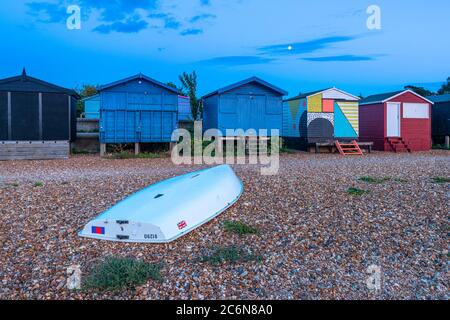 Moonrise behind the colourful beach huts on West Beach in Whitstable, Kent. Stock Photo