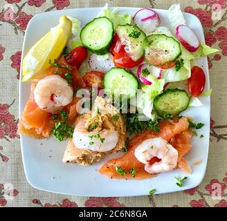 Deluxe seafood salad of crab, smoked salmon and prawns, with a green salad, a wedge of lemon and ready to eat Stock Photo