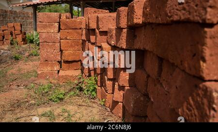 Stacks of bricks in yard. Shabby red bricks stacked on sandy ground with grass on sunny day in yard Stock Photo