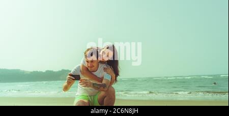 Happy couple taking selfies near sea. Loving couple embracing during date on beach against waving sea and cloudless sky. Stock Photo