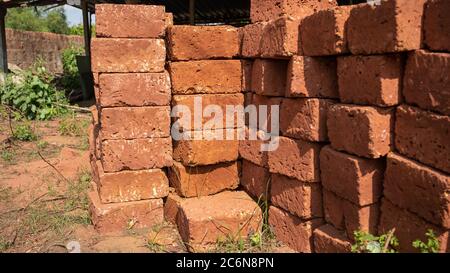 Stacks of bricks in yard. Shabby red bricks stacked on sandy ground with grass on sunny day in yard Stock Photo