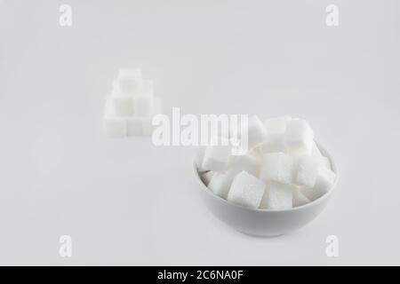 Sugar cubes in a white bowl, with a few sugar pieces stacked next to each other Stock Photo