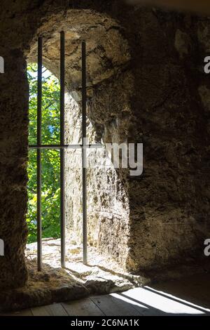 Prsion window with iron bars in stone wall with the view of spring time outside Stock Photo