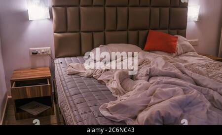 An empty rumpled bed in the hotel. Crumpled blanket and pillows. Close-up of messy bed. Used linens, bed sheet and pillows after sleeping in the night Stock Photo