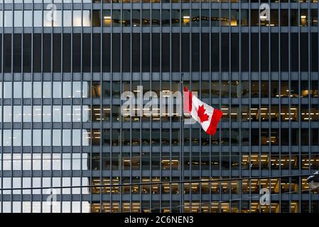 Canadian flag in front of a modern office building at dusk downtown Toronto, with illuminated office spaces. Stock Photo