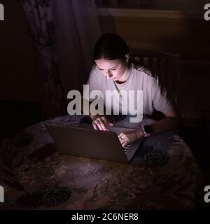 Woman freelancer working on laptop late at night at home, sharing social media. Distance job Stock Photo