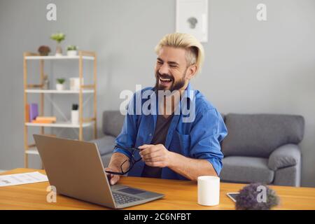 Laughing male freelancer using laptop vide chat conference at home. Stock Photo