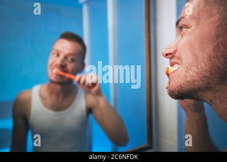 Morning hygiene routine. Man brushing teeth and looking in mirror of home bathroom. Stock Photo