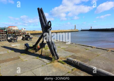 A very old and large Ships Anchor displayed on a pier with Whitby Harbour in the Background. North Yorkshire, England, UK Stock Photo