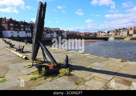 A very old and large Ships Anchor displayed on a pier with Whitby in the Background. North Yorkshire, England, UK Stock Photo