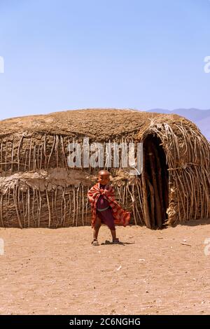 Serengeti, Tanzania - September 21. 2012: A smilding Massai young boy in red in front of the traditional huts inside an Massai village in the Serenget Stock Photo