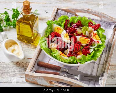 close-up of baby octopus salad with hard-boiled eggs, capers, marinated onion on lettuce leaves in a bowl on a tray, on a rustic wooden table with oli Stock Photo