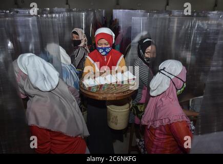 Malang, Indonesia. 11th July, 2020. Workers package cigarettes at Gudang Baru cigarette factory in Malang, East Java, Indonesia, July 11, 2020. Workers wearing face masks work with bordering plastic shields amid the COVID-19 outbreak. Credit: Aman R./Xinhua/Alamy Live News Stock Photo