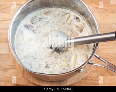 Cream soup in a pan. Blender portion in the soup. Grind puree soup ingredients. Pieces of mushrooms and potatoes. Stock Photo