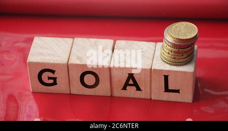 Goal on wooden cubes and stcack of coins on red. Target business career concept Stock Photo