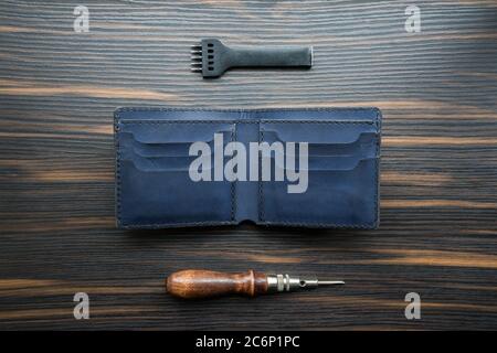 handmade blue leather wallet, punch and awl on a wooden table.  Stock Photo
