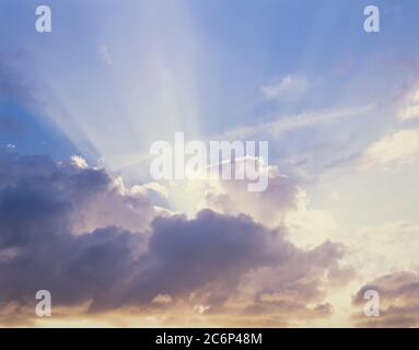 Sun rays coming out from behind clouds with blue sky above Stock Photo