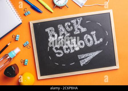 Stationery school supplies around the board with the words Back to school. Orange background, top view. Stock Photo