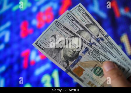 Investment withdrawal concept: View on hand holding three 100 dollar notes, blurred stock market exchange board background. (Focus on face) Stock Photo