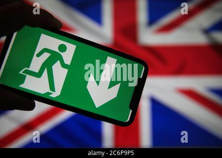 Viersen, Germany - July 9. 2020: View on isolated mobile phone screen with green emergency evacuation exit sign. Blurred union jack background. Stock Photo