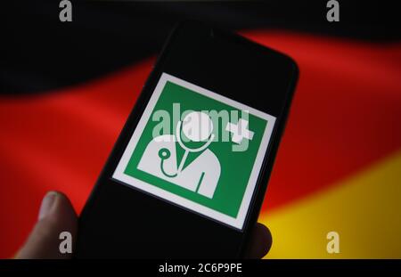 Viersen, Germany - July 9. 2020: View on isolated mobile phone screen with international health and medical doctor symbol. Blurred waving german flag Stock Photo