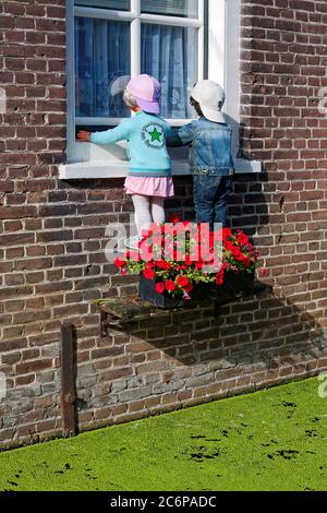 manequins looking into window, boy, girl, children, flower box, canal green with algae, cute, humorous, brick building, Europe, Willemstad; Netherland Stock Photo