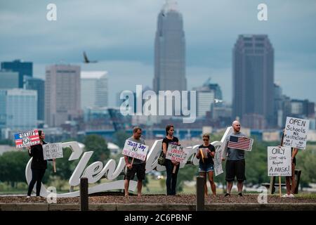 Cleveland, Ohio, USA. 11th July, 2020. People are seen at the Cleveland Script Sign during a 'Mask Mandate Protest,'' hosted by TERESA MCINNIS WHITE (far left) and KEVIN FREEMAN (third from right) Saturday, July 11, 2020 at Edgewater Park, in Cleveland, Ohio. The City of Cleveland and Cuyahoga County is currently under a red alert, according to the Ohio Public Health Advisory System, which advises wearing a mask while in public and other congregate areas. Governor Mike DeWine enacted the new map-based color coded alert system that helps highlight hot COVID hotspots on a county by county basi Stock Photo