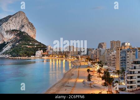 Panoramic view from above of Calpe cityscape. Street lights illuminating seafront promenade during sunset. Empty sandy beach and rocky mountain Ifach Stock Photo