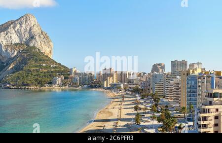 Sandy beach with parasols and vacationers, Penyal d'Ifac Natural Park view. Turquoise blue Sea water summer day. Seafront promenade of Calpe spanish r Stock Photo