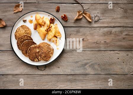 Autumn breakfast - pancakes with caramelized apples, pecan nuts and honey on wooden table, top view, copy space. Healthy seasonal vegetarian meal. Stock Photo