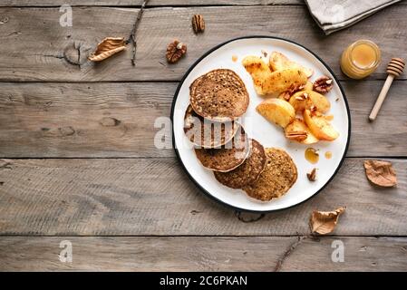 Autumn breakfast - pancakes with caramelized apples, pecan nuts and honey on wooden table, top view, copy space. Healthy seasonal vegetarian meal. Stock Photo