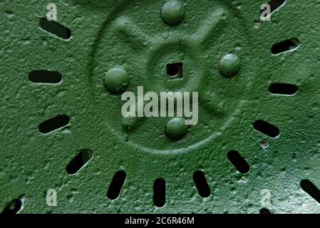 Closeup of an antique steel tractor seat painted green.  Perforations in the seat create an abstract pattern. Stock Photo