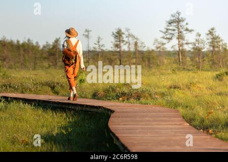 Woman botanist with backpack on ecological hiking trail in summer outdoors. Naturalist exploring wildlife and ecotourism adventure walking on path thr Stock Photo