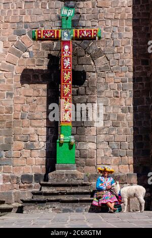 Peruvian native indigenous woman wearing traditional clothing with an alpaca, Convento de San Francisco de Asis de Cusco, cross, crucifix, Peru Stock Photo