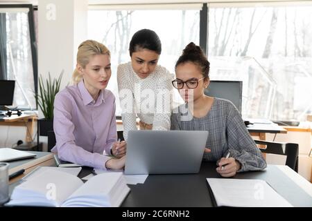 Focused multiracial female employees work on laptop together Stock Photo