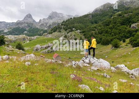 žmother and son standing on the rock on a meadow near Bukumirsko lake with a view over the mountains, Montenegro Stock Photo