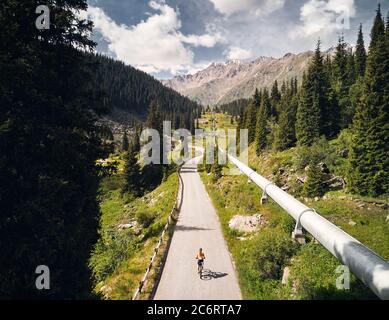 Man on mountain bike rides on the road to the mountain valley against blue cloudy sky. Recreation and healthy lifestyle concept. Stock Photo