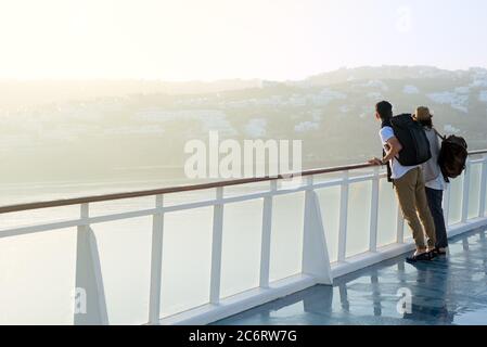 Young couple with backpacks watch misty coast standing on a ship deck Stock Photo