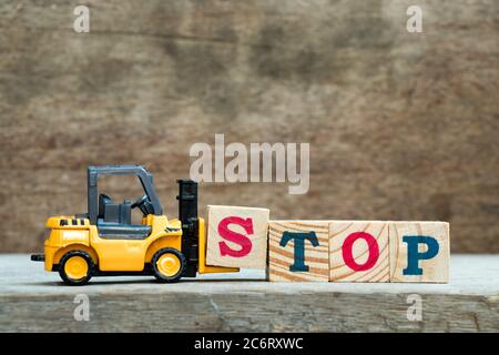 Yellow toy forklift hold letter block S to complete word stop on wood background Stock Photo