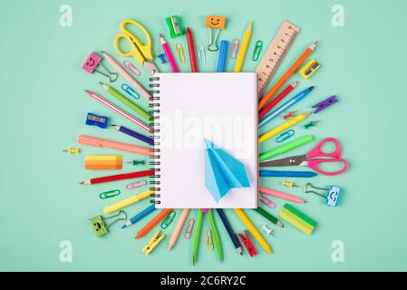 Top above overhead view photo of multicolored stationery and blank notebook with blue paper plane isolated on turquoise background Stock Photo