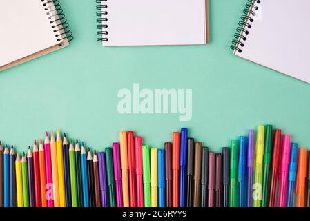 Back to school concept. Top above overhead view photo of colorful crayons pens markers and blank notebooks isolated on turquoise background Stock Photo