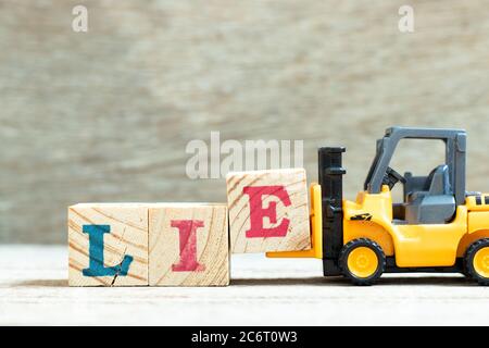 Toy forklift hold letter block e to complete word lie on wood background Stock Photo