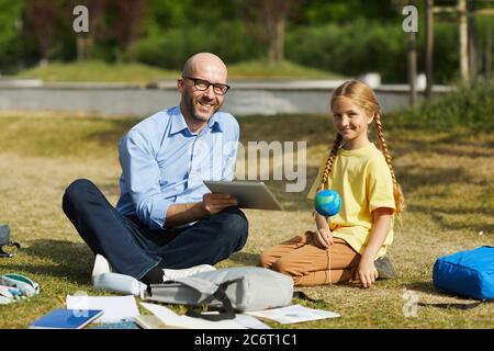 Full length portrait of smiling bald teacher looking at camera while enjoying outdoor astronomy lesson with cute blonde girl, copy space Stock Photo