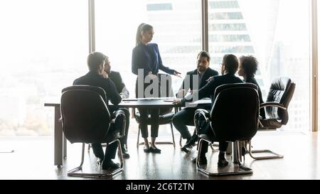 Young business woman standing at table, talking to diverse colleagues. Stock Photo