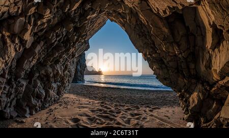 view from the stone cave on the sunset, sea and the beach, the volcanic rock of the cave is lit by the warm setting sun. volcanic basalt as in Iceland Stock Photo